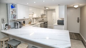 A modern kitchen with a large marble island, bar stools, and a microwave. - Oceanfront & Pool, on the Boardwalk at 37th Street (Virginia Beach)
