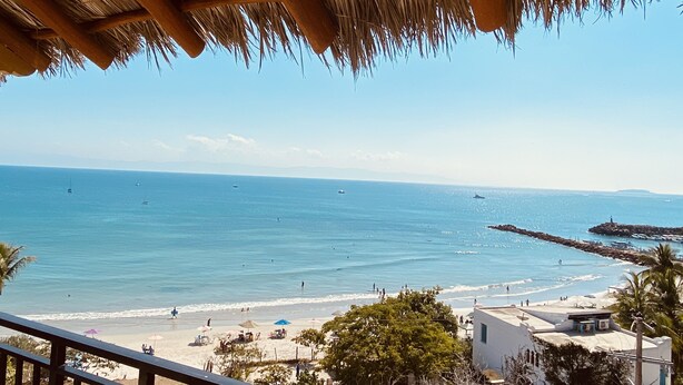 A beach with a thatched roof structure, clear blue sea, and a few boats.
