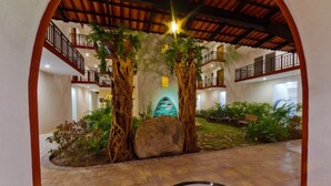 An indoor atrium with a central tree, stone pathway, and a tiled floor.