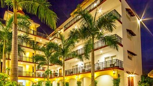 A hotel with a swimming pool, palm trees, and multiple balconies.