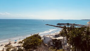 A coastal beach scene with clear skies, a sandy shore, and a rocky breakwater.