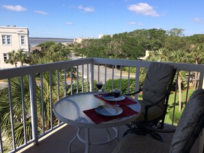 Enjoy a romantic dinner for two on this balcony overlooking a serene landscape with palm trees and a distant shoreline.