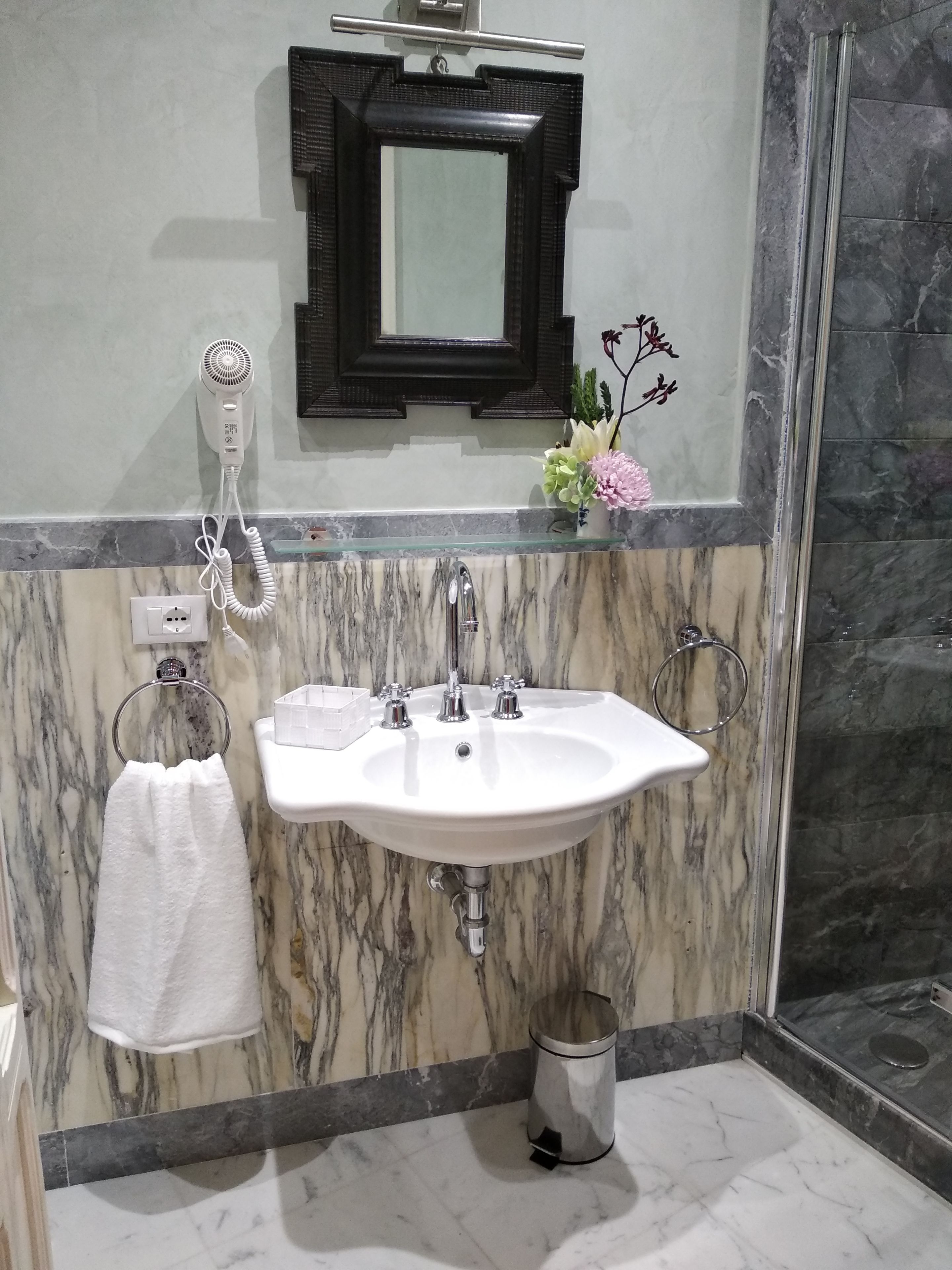 A bathroom with a marble sink, a towel rack, a hairdryer, a mirror, and a trash bin.