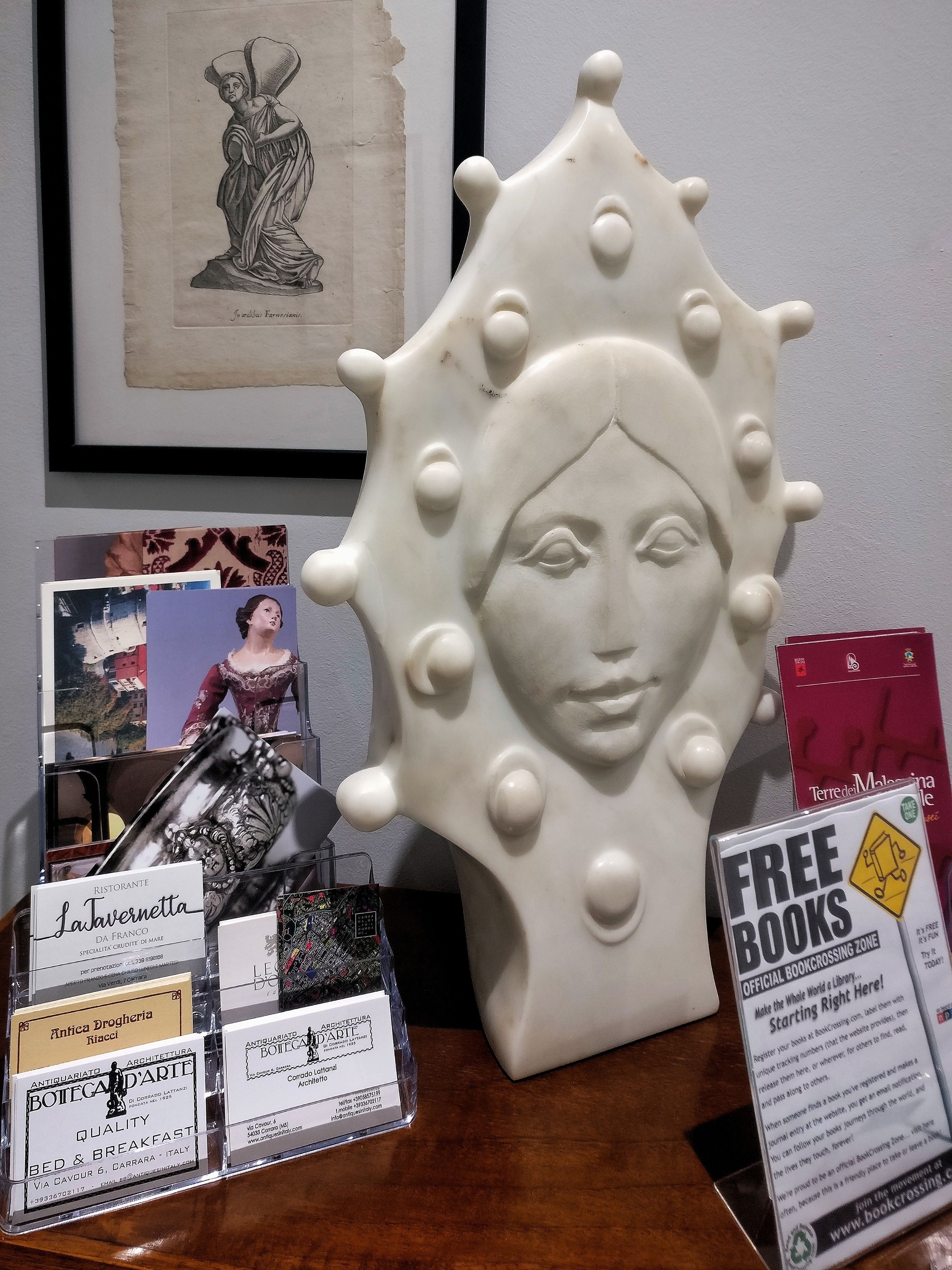 A table with a white ceramic sculpture, framed artwork, and various business cards.