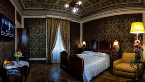 Ein Hotelzimmer mit einem großen Bett, einem Sessel, einem Tisch mit Blumenvase, einem Nachttisch mit Lampe und einem an der Wand montierten Fernseher, der eine Frühstücks-Werbung zeigt.