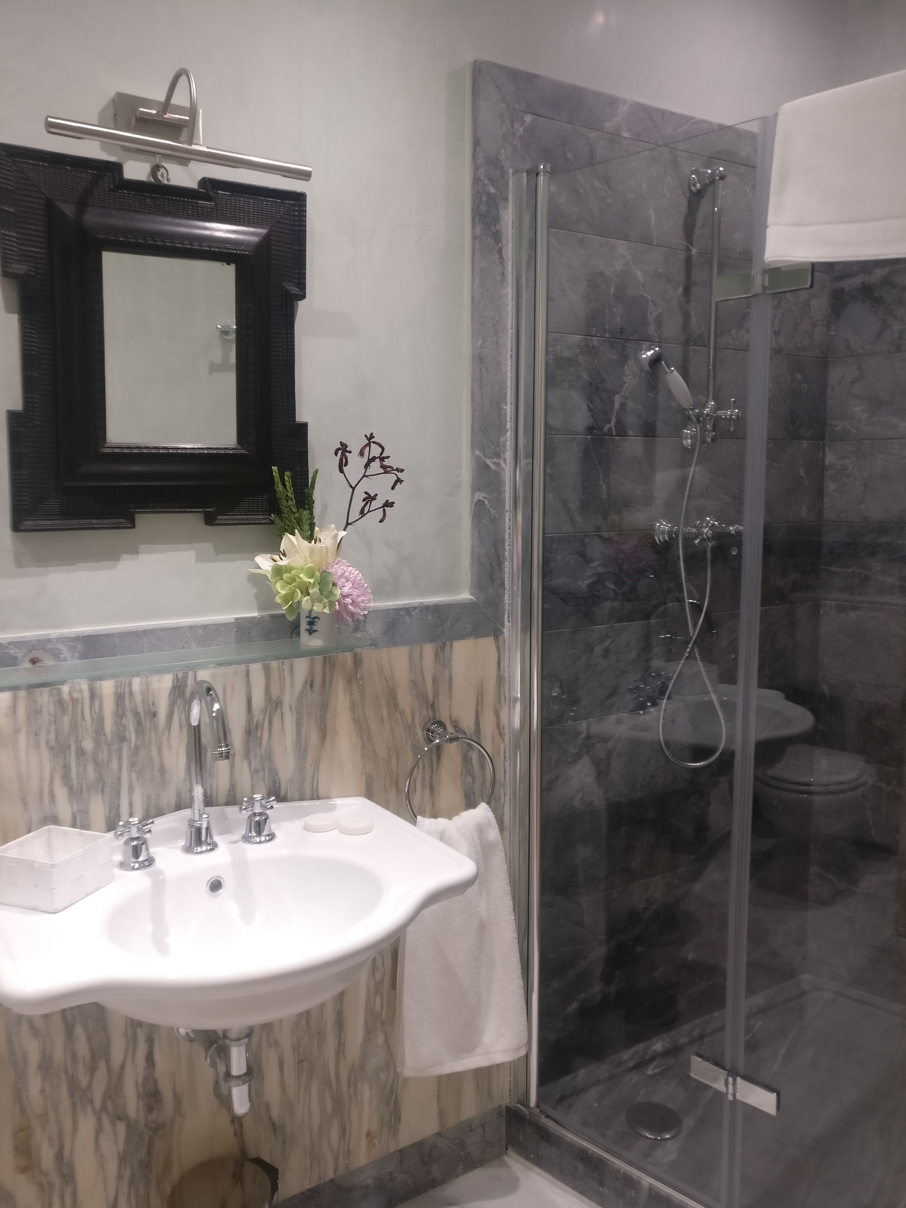 Un baño con lavamanos de mármol, ducha con mampara de vidrio y un espejo sobre el lavamanos.