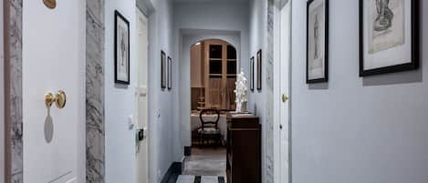 A hallway with marble flooring, framed artwork on the walls, and a door with a nameplate.