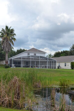 A house with a large covered outdoor area, a pond, and a palm tree. - Family-Friendly Vacation Villa Near Disney – Space, Comfort & Fun for Everyone (Clermont)