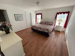 A bedroom with a large bed, a dresser, a nightstand, a window with curtains, and a door. - Family-Friendly Vacation Villa Near Disney – Space, Comfort & Fun for Everyone (Clermont)