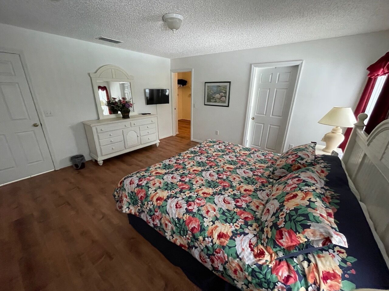 Une chambre à coucher avec une couvre-lit à motifs floraux, une commode, un miroir et un téléviseur.