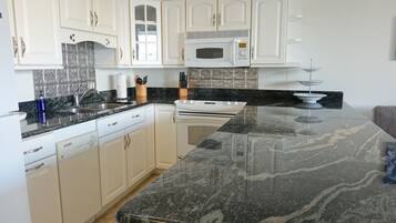A modern kitchen with white cabinets, a black marble countertop, a built-in microwave, and a stove.