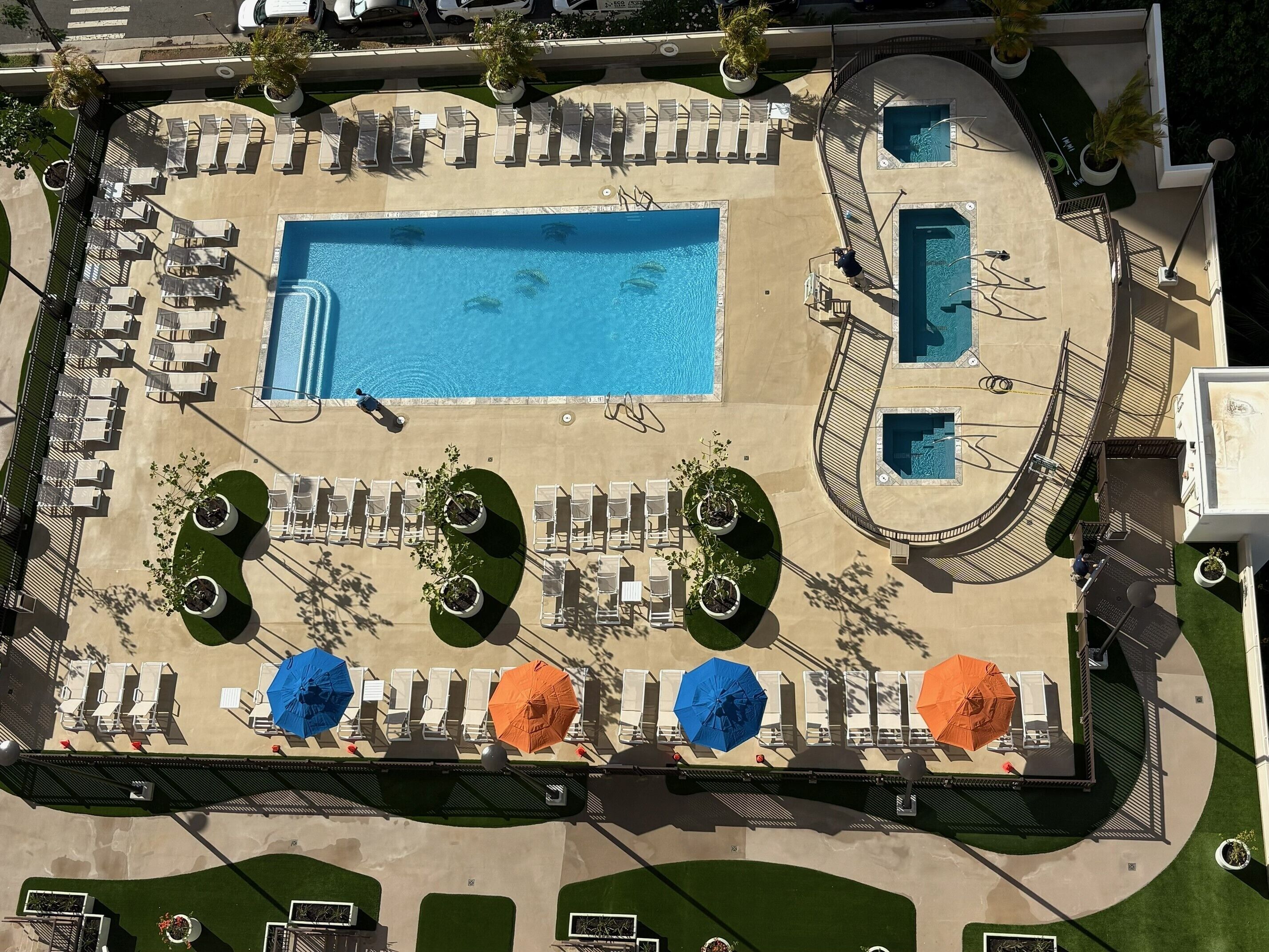 An aerial view of a resort with a large central pool, multiple smaller pools, and numerous sun loungers and umbrellas.