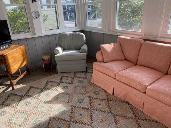Un saló acollidor amb un butac armchair gris, un sofà de color préssec i una catifes amb dibuixos.