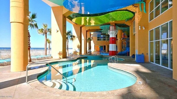A pool area with a clear view of the ocean, a lifeguard tower, and a covered seating area with palm trees. - Splash resort - Beachfront - Family-friendly - Optional beach services and more! (Panama City Beach)