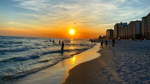 A beach with a sunset, waves, and high-rise buildings in the background. - Splash resort - Beachfront - Family-friendly - Optional beach services and more! (Panama City Beach)