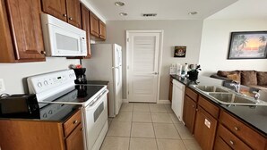 A kitchen with wooden cabinets, a white stove, a microwave, a refrigerator, and a dishwasher. - Splash resort - Beachfront - Family-friendly - Optional beach services and more! (Panama City Beach)