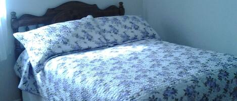 A bedroom with a bed, a wooden headboard, a framed picture on the wall, and a tiled floor.