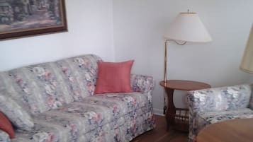 En stue med en blomstret sofa, en rød pude, et træsofabord og en gulvlampe.