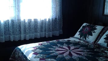 A bedroom with a large bed, a window with lace curtains, and a dark wooden wall.