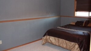 Een slaapkamer met een bed, een raam met jaloezieën en een vloerbedekking.