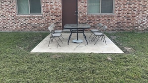 Una casa in mattoni con un patio attrezzato con tavolo e quattro sedie, un ombrellone e un piccolo tavolino rotondo.