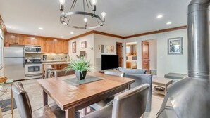 Une cuisine moderne avec des meubles en bois, des appareils électroménagers en acier inoxydable et un coin repas comprenant une table en bois et des chaises en cuir.