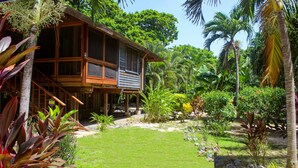 Une maison en bois dotée d’un balcon, entourée d’une végétation tropicale luxuriante.