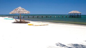 Une plage avec des parasols en chaume, des chaises longues et une jetée qui s’avance dans la mer.