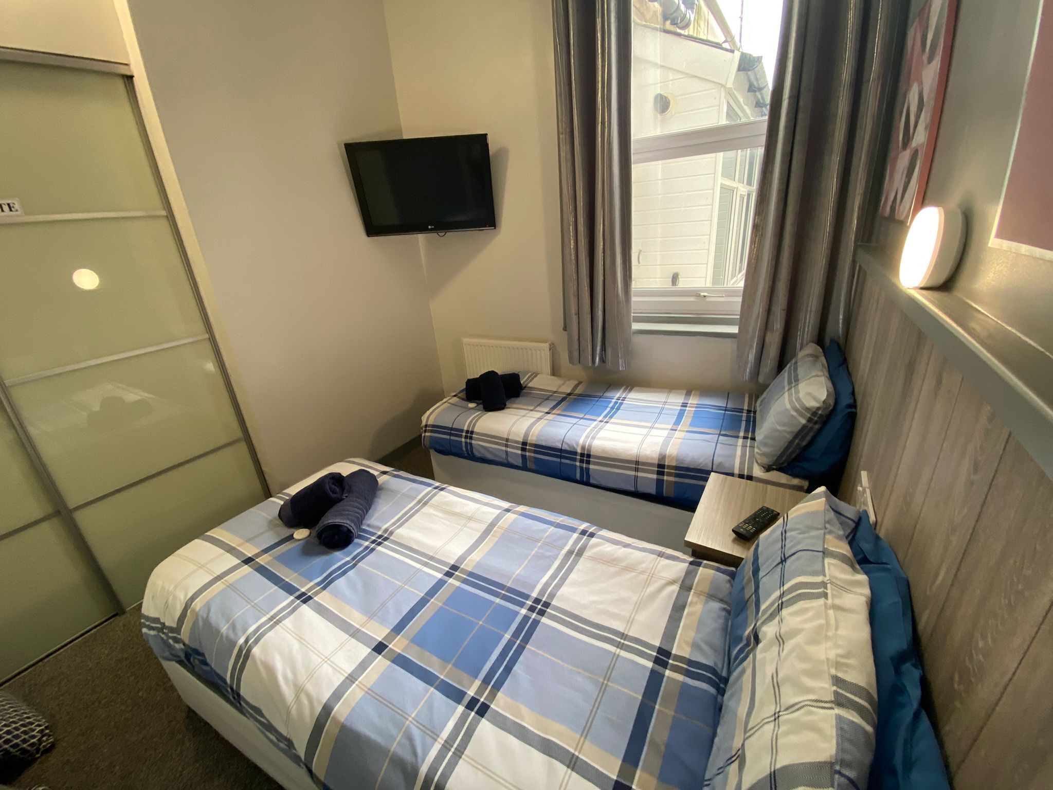 Une chambre d’hôtel avec deux lits, une télévision, une fenêtre avec des rideaux et une armoire.