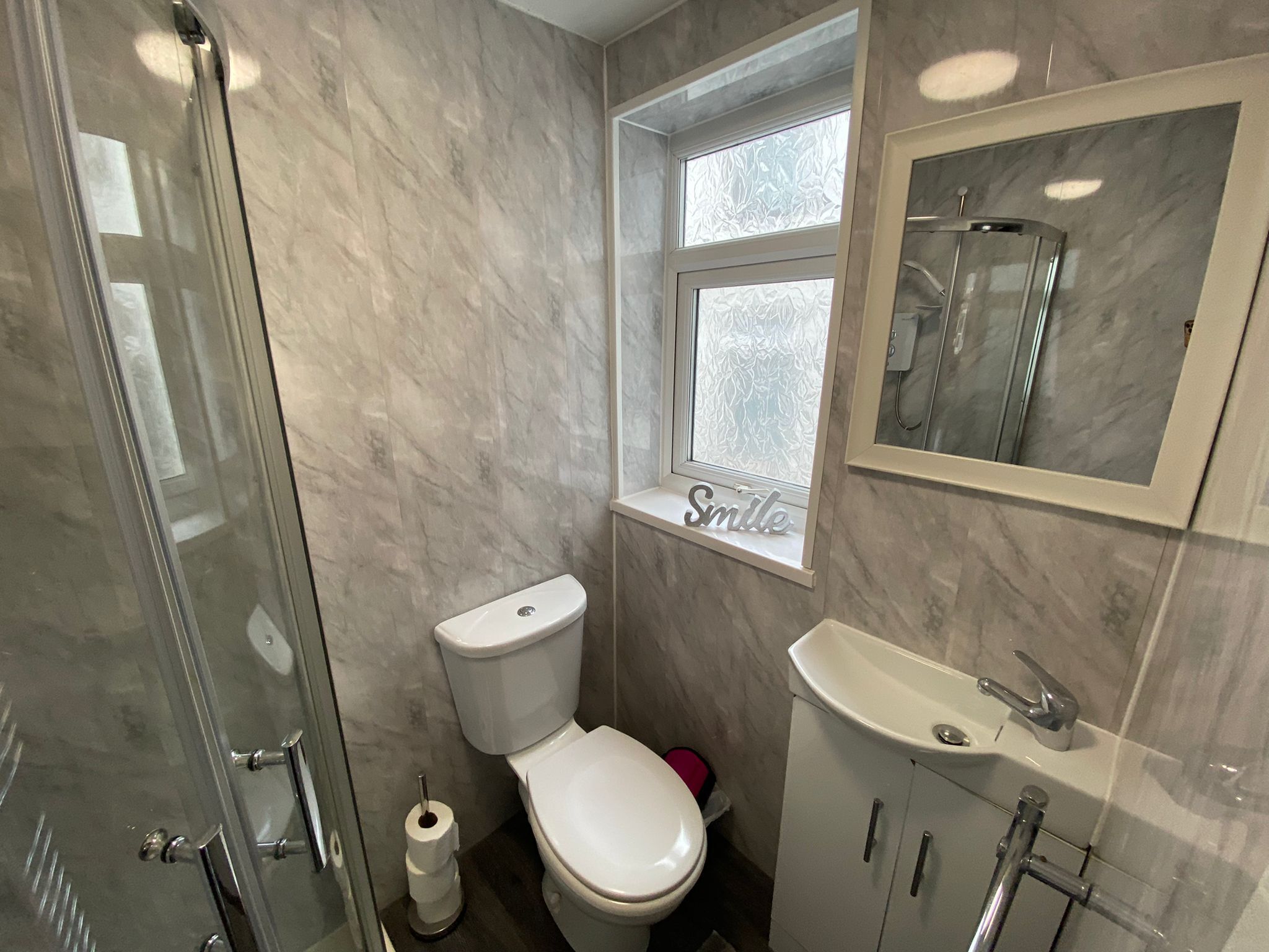 A bathroom with a toilet, a sink, a shower, and a window with frosted glass.