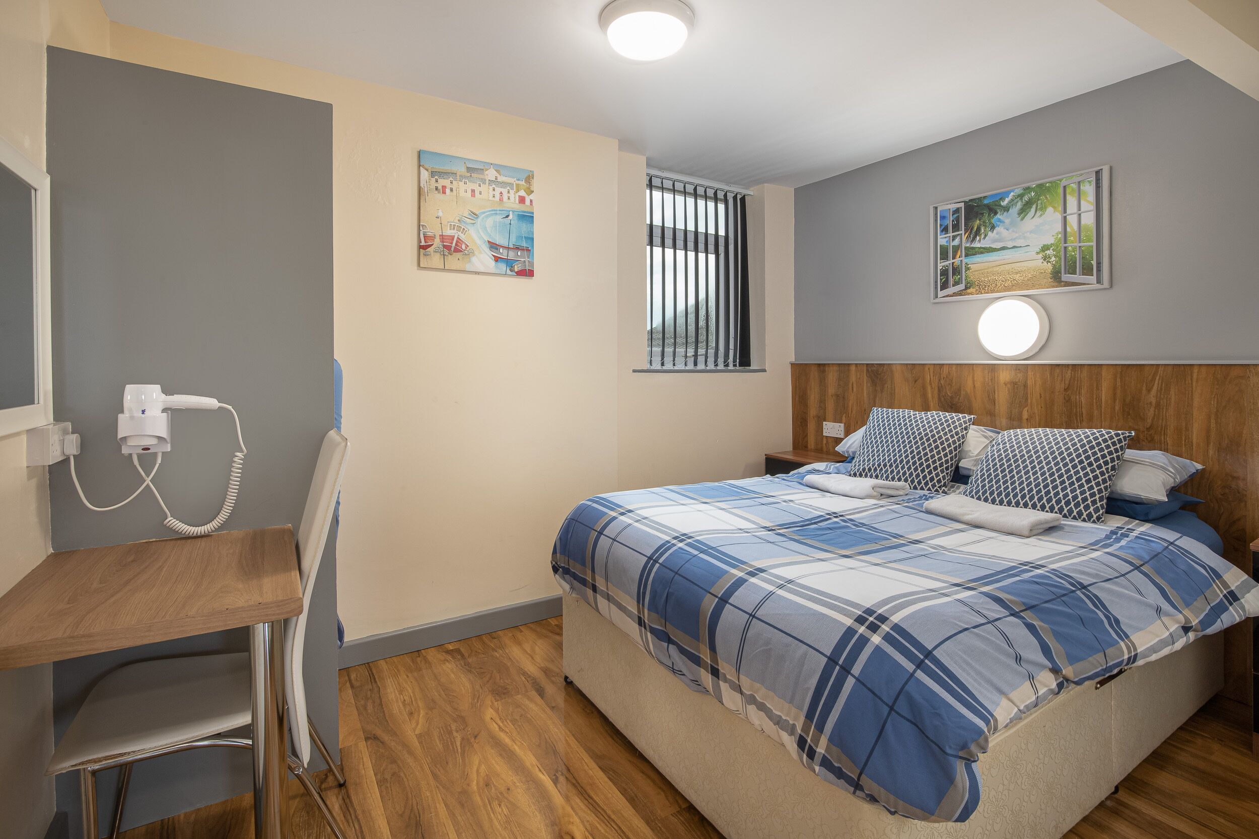 Ein Schlafzimmer mit einem Bett, einem Schreibtisch, einem Stuhl, einem Fenster mit Jalousien und zwei Wandleuchten.