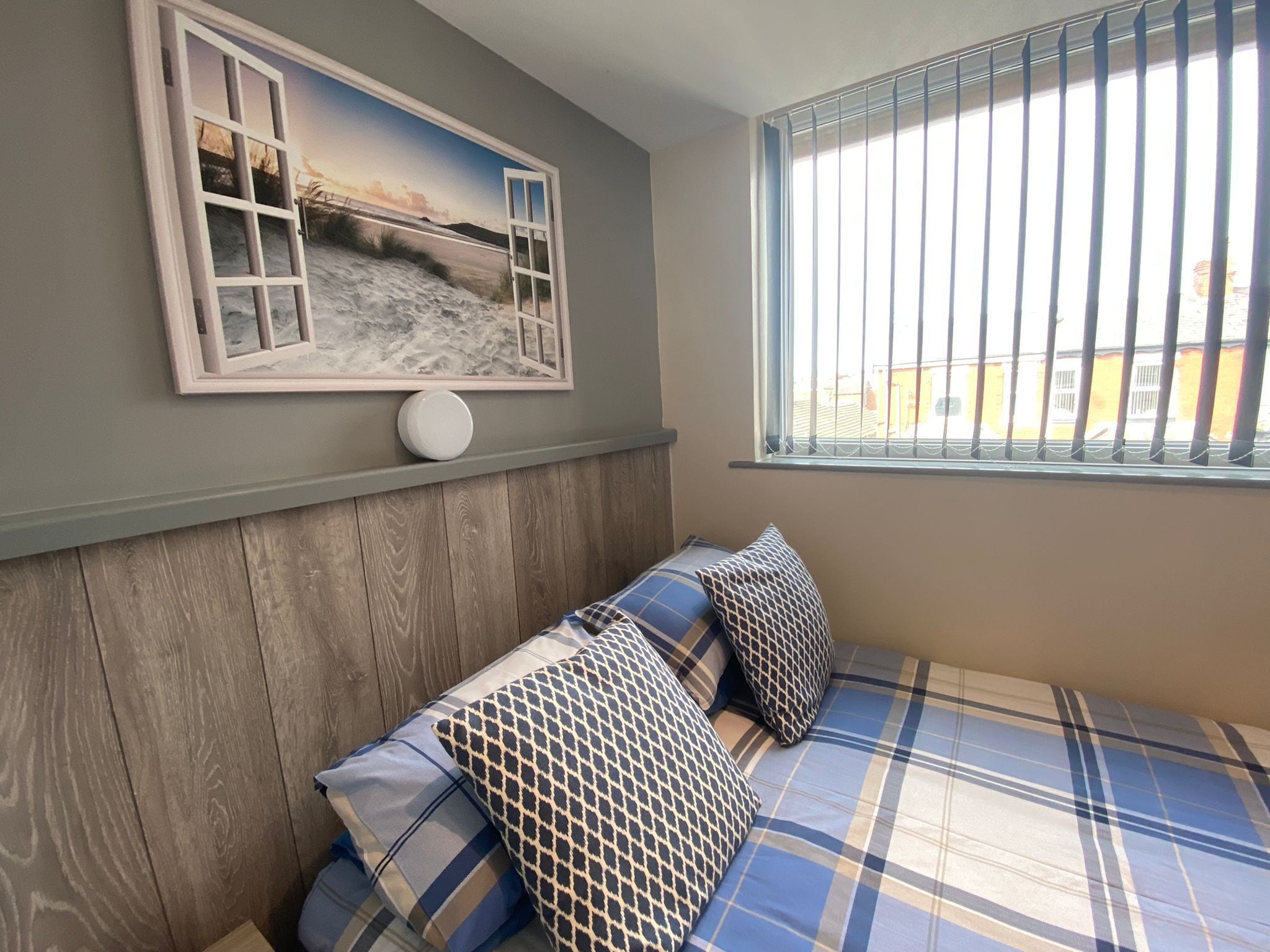 A bedroom with a bed, pillows, a framed picture, and a window with blinds.