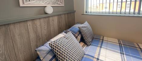 A bedroom with a bed, pillows, a framed picture, and a window with blinds.