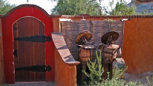 Un portail rustique avec une arche rouge et une porte en bois, qui mène à un chemin pavé de briques.