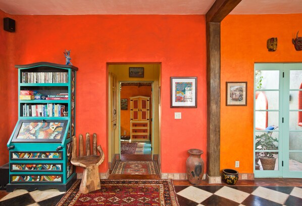 Een kamer met een zwart-wit geruite vloer, een houten stoel in de vorm van een hand, een boekenplank en een deur naar een andere kamer.