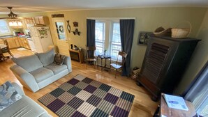 Una sala de estar con un sofá, una mesa de centro y una televisión. Se ve una cocina al fondo, con un refrigerador y alacenas.