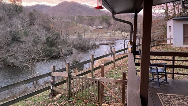 Una terraza de madera con vista a un río y una ladera boscosa.