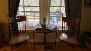 Una habitación con dos sillas de madera y una mesita, una ventana con cortinas, y vistas al exterior.