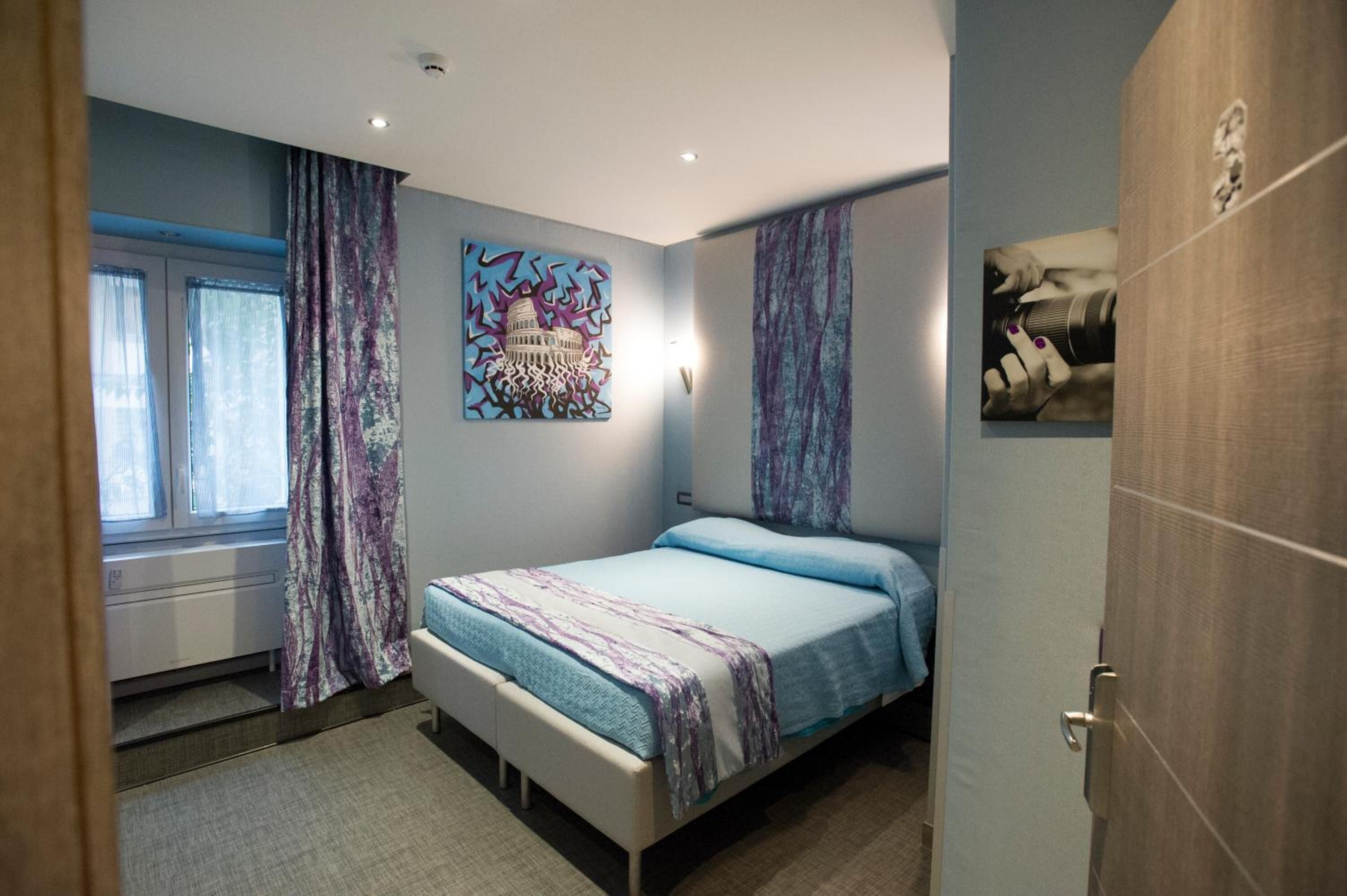 A bedroom with a bed, curtains, a window, and artwork on the walls.