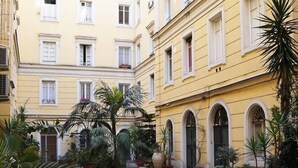 A courtyard with potted plants and a tiled floor, surrounded by yellow buildings with arched windows. - Gracchi Guest House (Rome)