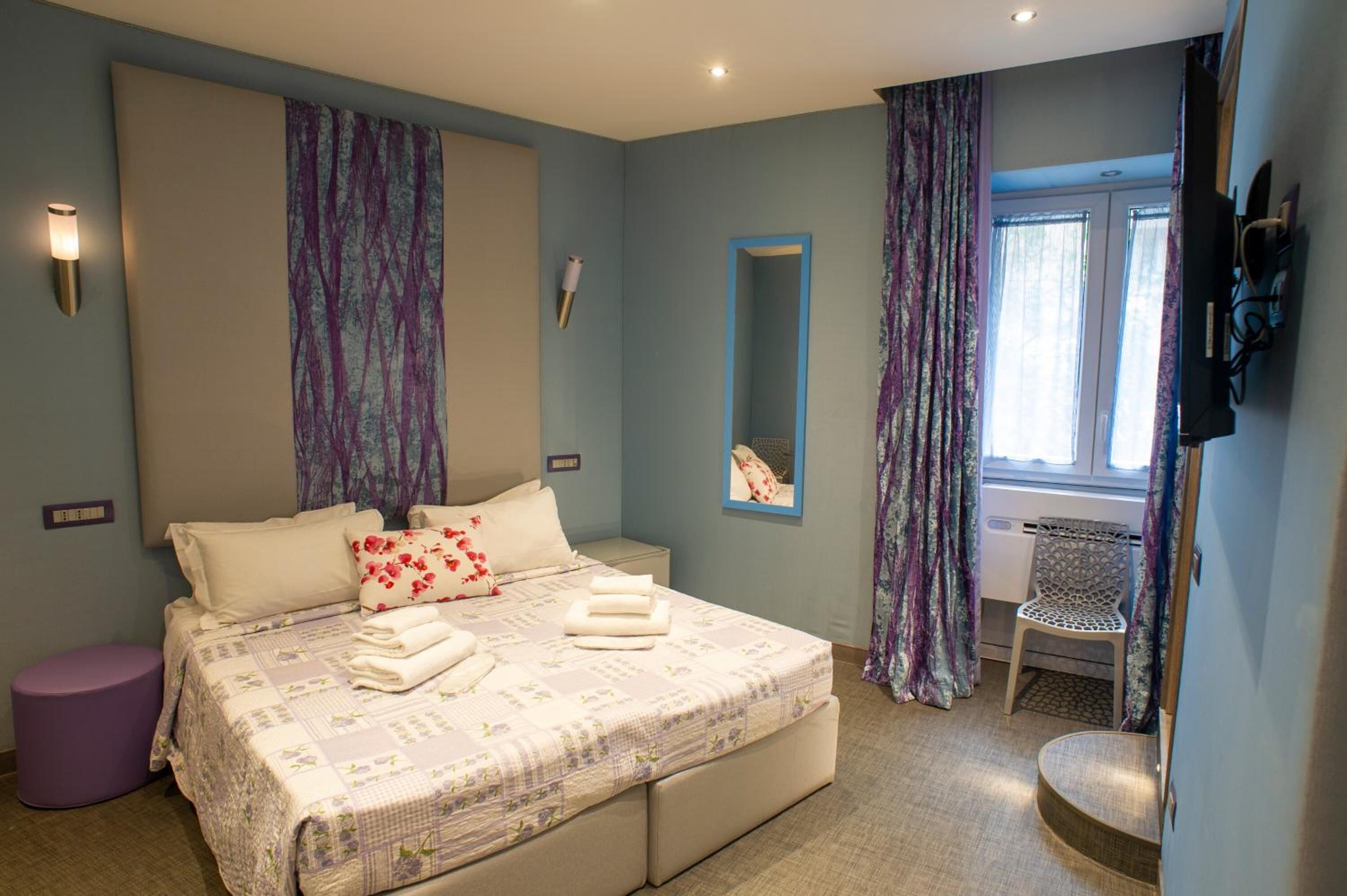 A bedroom with a bed, a chair, a mirror, and a window with curtains.