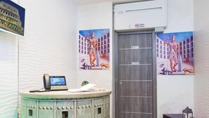 A reception area with a round counter, a grey door, and two wall paintings of a man in a coliseum. - Gracchi Guest House (Rome)