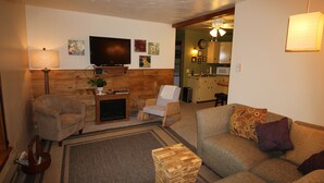 A living room with a television, two armchairs, a sofa, and a wooden coffee table.