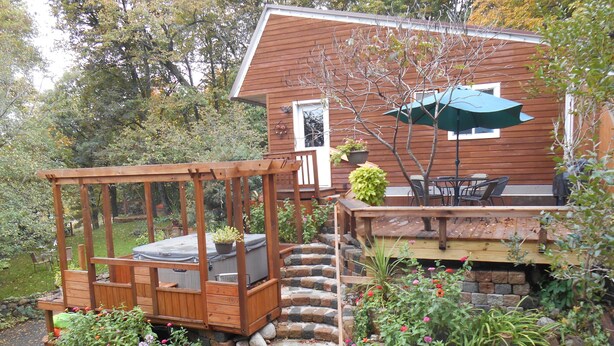 A wooden deck with a built-in seating area, a stone pathway leading to a wooden staircase, and a patio with outdoor furniture.
