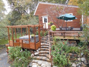A wooden deck with a built-in seating area, a stone pathway leading to a wooden staircase, and a patio with outdoor furniture.