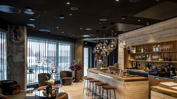 Zona de bar moderna con mostrador de madera, taburetes y diferentes tipos de copas.