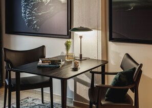 Una habitación moderna con una mesa de madera oscura, dos sillas negras, una lámpara de pie y un cuadro enmarcado en la pared.