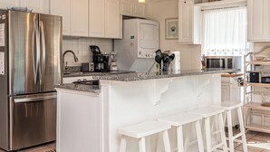 A modern kitchen with white cabinets, stainless steel appliances, and a central island with bar stools. - Unique Beach Cottage with pool and easy beach access (Gulf Shores)