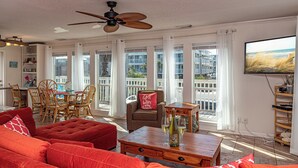 A spacious living room with a red sofa, wooden coffee table, and a ceiling fan. - Unique Beach Cottage with pool and easy beach access (Gulf Shores)