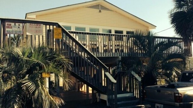 A two-story building with a balcony, palm trees, and a truck parked in front. - Unique Beach Cottage with pool and easy beach access (Gulf Shores)